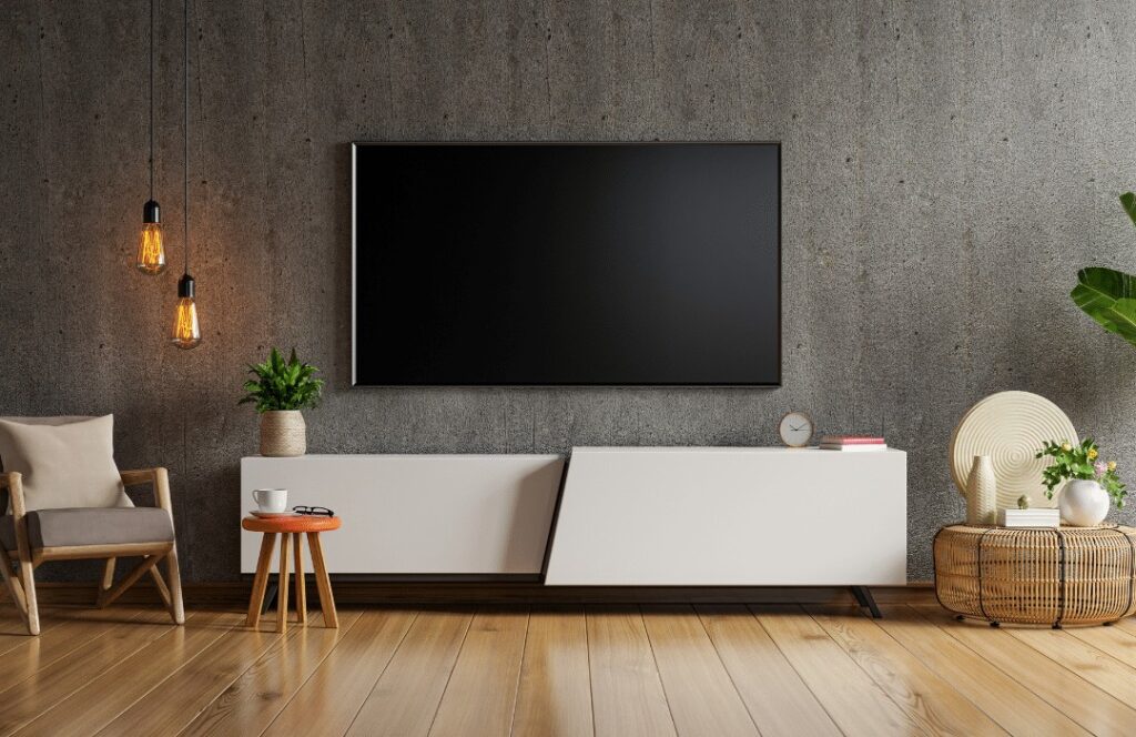 Modern living room in TN with a large flat-screen TV on a concrete wall, white TV console, armchair, side table with a cup, hanging lights, green plants, and wooden floors—perfectly finished by a handyman Davidson & Williamson County trusts.
