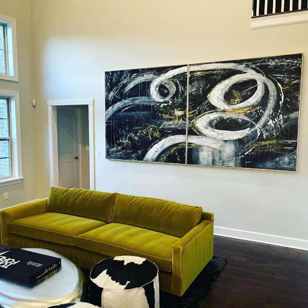 A modern living room with a mustard yellow sofa, black and white abstract artwork, round coffee table, and ottoman on a dark rug. Large windows let in natural light—expertly finished by a handyman in Davidson & Williamson County, TN.