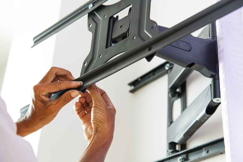 A person’s hands installing a black TV wall mount bracket on a white wall, adjusting or securing one of its components—just the type of task for a skilled handyman in Davidson & Williamson County, TN.